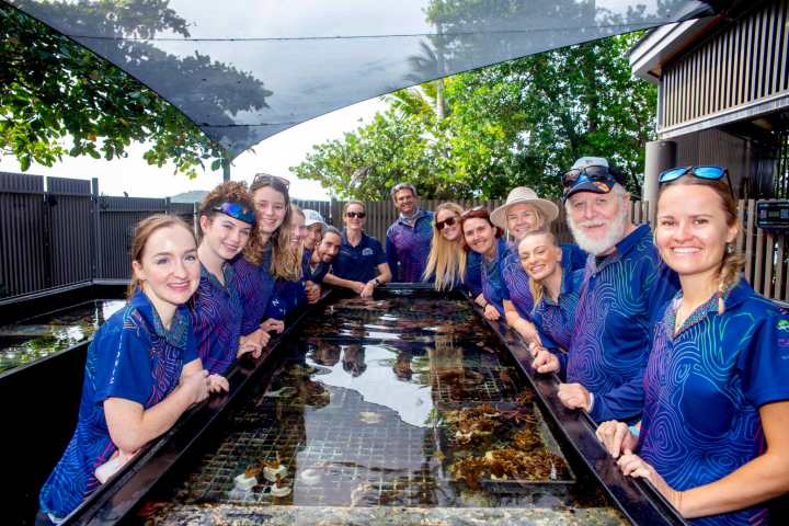 Group of people smiling around a large aquarium tank outdoors.