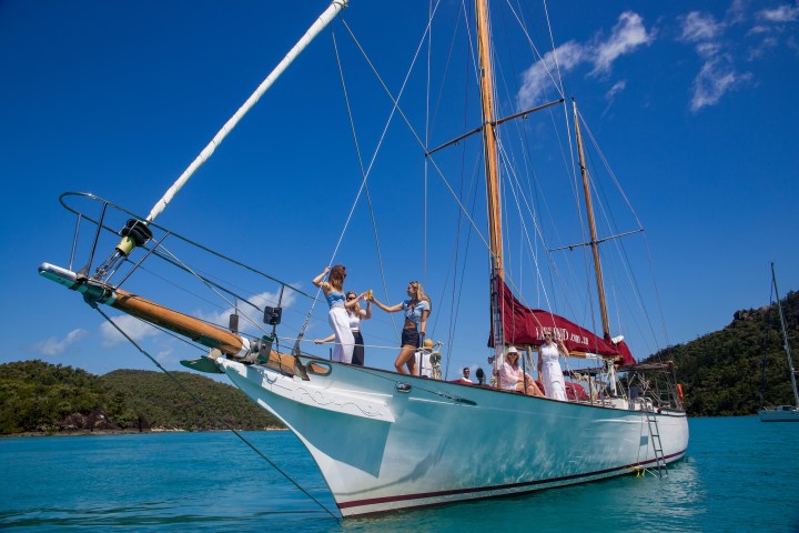 Sailing yacht Lady Enid in Nara Inlet, Hook Island, Whitsundays with girls on the bow toasting sparkling wine