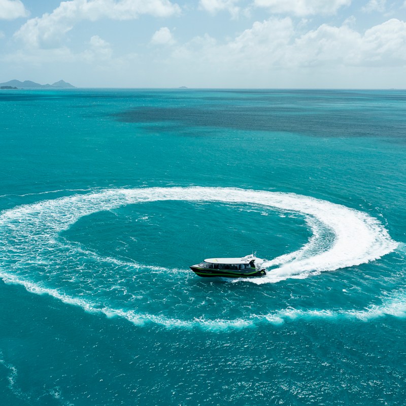 a man riding a wave on top of a body of water with Lady Elliot Island in the background