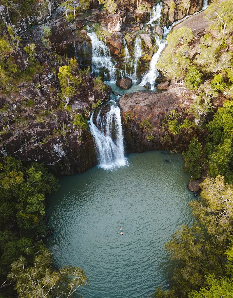 Cedar-Creek-Falls-Aerial-Tourism-and-Events-Queensland_1 a large waterfall next to a rock