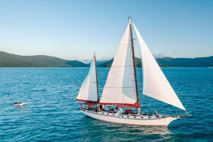 Sailboat with white sails on a blue lake surrounded by mountains.